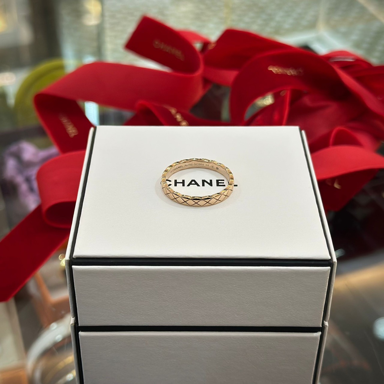 A Chanel Coco Crush quilted ring in beige gold presented on a Chanel box with a red ribbon